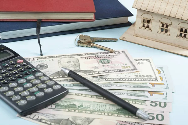 Ev tasarruf, bütçe kavramı. Model ev, not defteri, kalem, hesap makinesi ve ahşap ofis resepsiyon masası üzerinde para.
