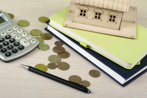 Ahorro en el hogar, concepto de presupuesto. Casa modelo, bloc de notas, calculadora, bolígrafo y monedas en mesa de escritorio de oficina de madera . — Foto de Stock