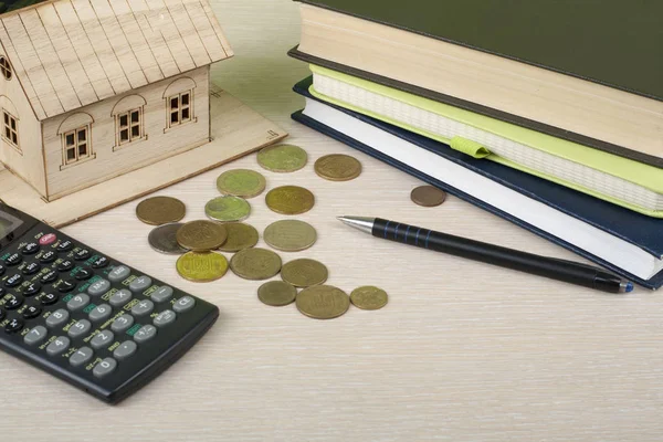 Ahorro en el hogar, concepto de presupuesto. Casa modelo, bloc de notas, calculadora, bolígrafo y monedas en mesa de escritorio de oficina de madera . — Foto de Stock