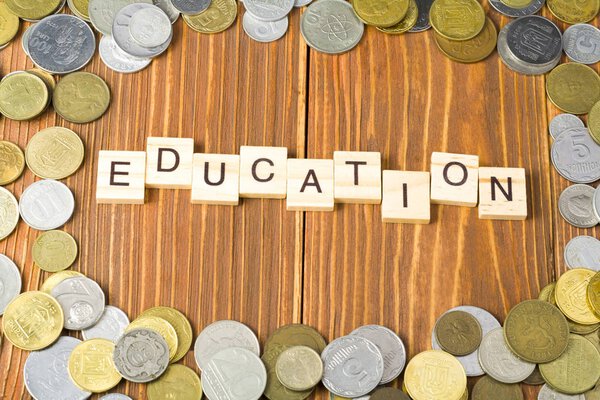 Слово ОБРАЗОВАНИЕ на деревянном кубе с рамой из монет на деревянном фоне
