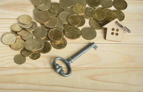Pojęcie nieruchomości lub nieruchomości na wynajem. Symbolem domu z kluczem i monety na podłoże drewniane. — Zdjęcie stockowe