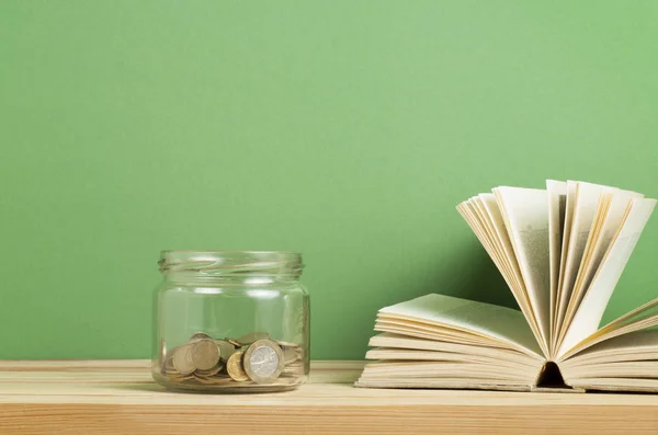 Κέρματα σε γυάλινο βάζο και ανοιχτό βιβλίο ξύλινο τραπέζι. Εξοικονόμηση, οικονομικών και Παιδείας έννοια. — Φωτογραφία Αρχείου