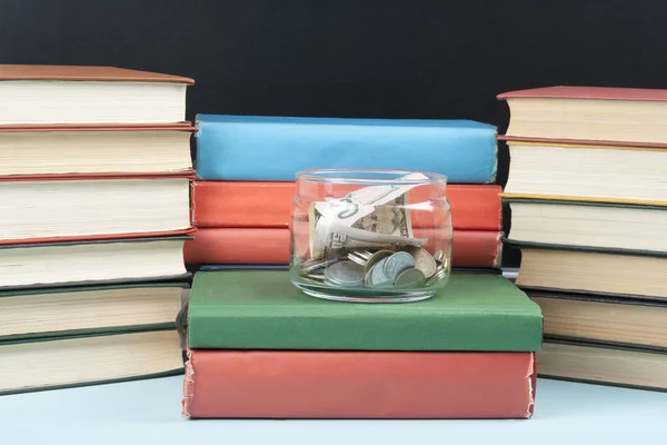 Χρήματα σε γυάλινο βάζο και στοίβα των βιβλίων πάνω ξύλινο τραπέζι. Εξοικονόμηση, οικονομικών και Παιδείας έννοια. — Φωτογραφία Αρχείου