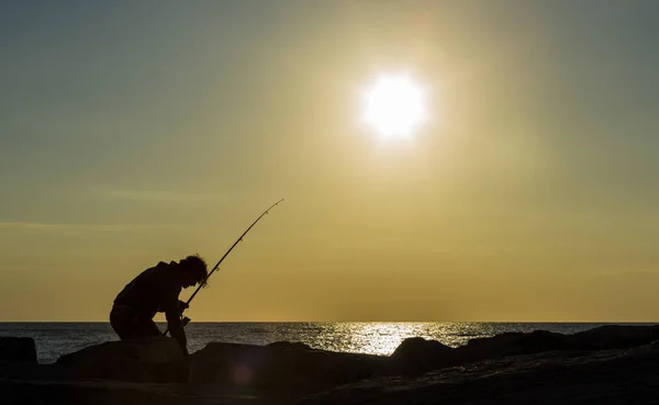 Hombre pescando en los primeros rayos de luz solar en la orilla del mar — Foto de Stock