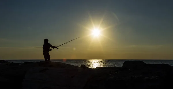 Man fishing in first rays of sunlight on sea shore Royalty Free Stock Photos