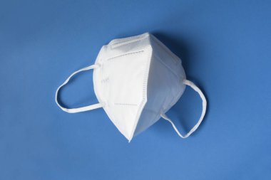Beyaz maskeli KN95 ya da N95 mavi arka planda koronavirüse karşı koruma sağlar. Virüslerin ve salgın COVID-19 'un yayılmasının önlenmesi.