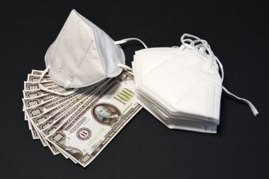 COVID-19 pandemik konseptinin maliyeti ffp2 veya KN95 önleme maskesi ve siyah arka planda 100 dolarlık banknotlar.