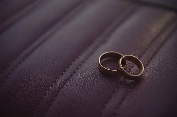 Wedding rings on a burgundy leather background inside the car — Stock Photo, Image