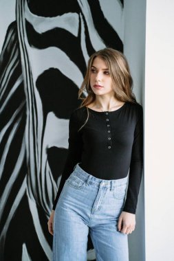 Sarışın, siyah tişörtlü ve arka planda zebra desenli kot pantolonlu güzel bir kızın portresi.