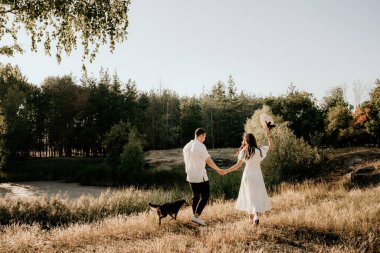 Genç çift yaz çayırlarında gün batımında yürüyor.