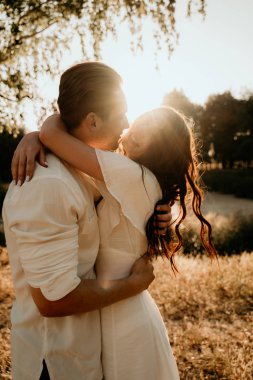 Genç çift yaz çayırlarında gün batımında yürüyor.