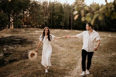 Genç çift yaz çayırlarında gün batımında yürüyor.