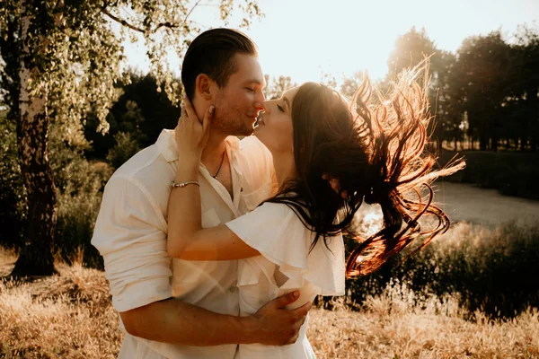 若い夫婦は日没時に夏の牧草地を歩きキスをし — ストック写真