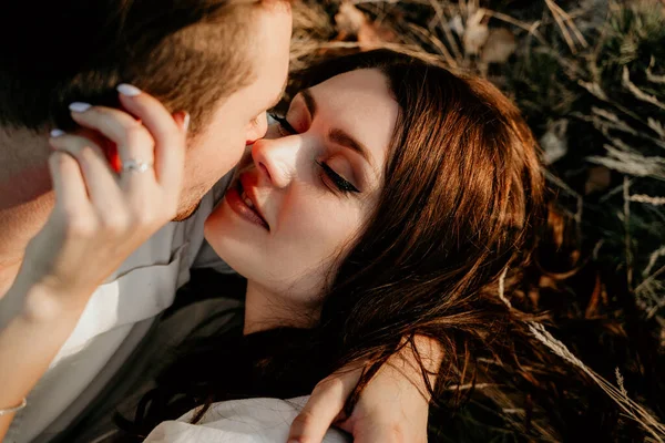 夏の日没時に草の上に寝そべってキスをするカップルが大好きです 軽装のブルネットの女の子 ラブストーリー — ストック写真