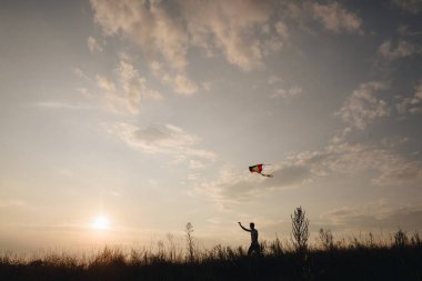 Adam tepede uçurtmayla koşuyor. Gün batımında bir adamın silueti. Güzel doğa..