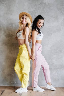 İki kız, bir esmer ve bir sarışın, renkli pantolonlu, hasır şapkalı. Kız arkadaşlar sarılıyor..