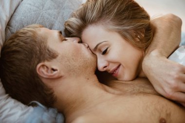 Yatak odasındaki çift yatak odasındaki yatakta. Pijamalı sarışın bir kız, çıplak gövdeli bir adam. Sevgiler ve sarılmalar. Güzel bir çift. Yılbaşı arifesi. Noel zamanı. Büyük bir çiftleşme battaniyesi.