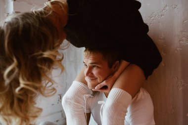 Bir çift sevgili, sarıl, öp, gül ve eğlen. Uzun siyah kazaklı ve beyaz yüksek golflü kız. Beyaz tişörtlü ve pantolonlu bir adam. Açık gri iç mekan, büyük pencere, kahverengi stil sandalye..