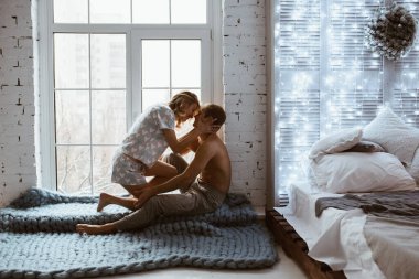 Parlayan yeni yıl çelenkleri. Şık bir iç mekan. Çift pencerenin yanında, mavi çiftleşme battaniyesinin altında. Nazikçe sarıl ve öp. Sarışın. Yer lambası. Atletik yapı. Kalpte gri pijama. Aşk hikayesi..