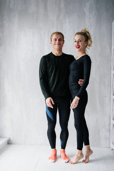 The guy and the girl in tracksuit. Black sports uniform. Male and female athletes. Pumped up body. Triathlon. Morning work-out. Set of exercises for body. Classes in pair. Workout together at home.