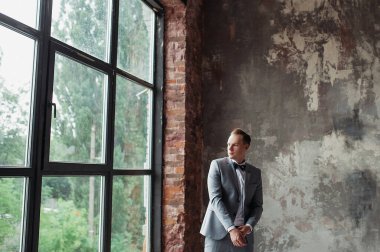 Damadın sabahı. Gelini bekliyoruz. Damat gri bir takım elbise ve papyonla gülümsüyor. Ceketini tamir eder ve pencereden dışarı bakar. Çatı katı tarzı bir oda..