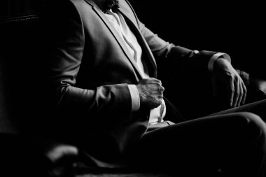 Bir adamın portresi. Gri takım elbiseli, beyaz gömlekli ve papyonlu damat kahverengi deri koltukta oturuyor. Çatı katı tarzı bir oda. Siyah beyaz fotoğraf