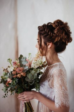 Gelin sabah şeffaf bir sabahlıkla toplanıyor. Pembeli çok güzel bir düğün buketi. Şık saç stili, örgülü örgüler..