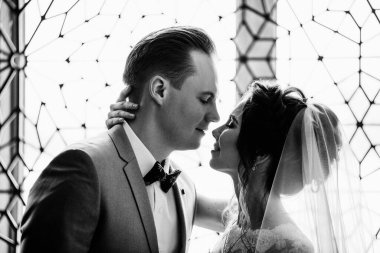 İlk buluşma. Damat elinde buketle gelinin odasına girer. Sarılırlar ve öpüşürler. Pembe gelinlik, gri takım elbise ve şık bir buket. Fas tarzında bir oda. siyah beyaz fotoğraf