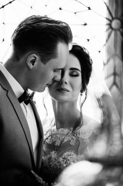 İlk buluşma. Damat elinde buketle gelinin odasına girer. Sarılırlar ve öpüşürler. Pembe gelinlik, gri takım elbise ve şık bir buket. Fas tarzında bir oda. siyah beyaz fotoğraf