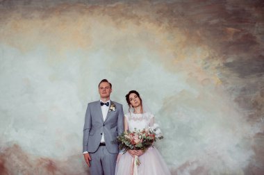 İlk buluşma. Damat elinde buketle gelinin odasına girer. Sarılırlar ve öpüşürler. Pembe gelinlik, gri takım elbise ve şık bir buket..