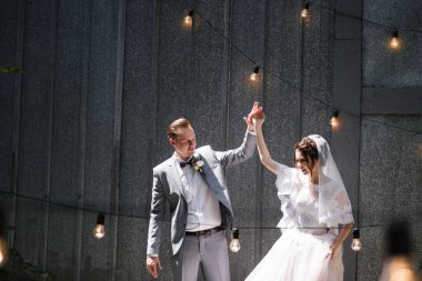 Gelin ve damat bahçede yürüyor. Ampullerden ve metal kapılardan oluşan bir çelengin önünde..