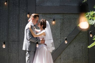 Gelin ve damat bahçede yürüyor. Ampullerden ve metal kapılardan oluşan bir çelengin önünde..