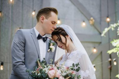 Gelin ve damat bahçede yürüyor. Ampullerden ve metal kapılardan oluşan bir çelengin önünde..