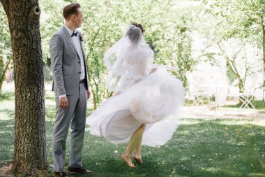 Gelin ve damat bahçede yürüyorlar. Ormanda düğün. Pembe, gür elbise ve gri takım elbise, papyon.