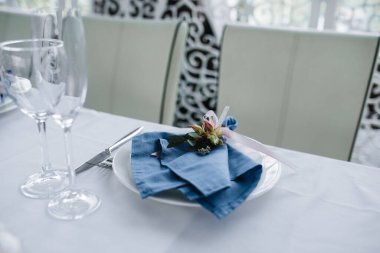 Mavi beyazlı düğün ziyafeti masasında servis edildi. Düğün dekorasyonu. Beyaz tabakta çiçekli mavi peçete..