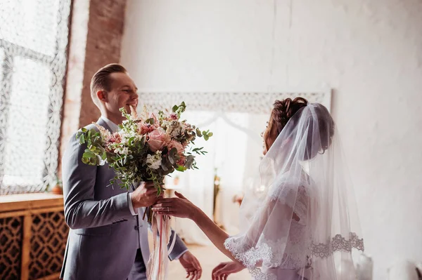 The first meeting. The groom comes into the room to the bride with a bouquet. Pink wedding dress, gray suit and stylish bouquet. Room in the style of Morocco.
