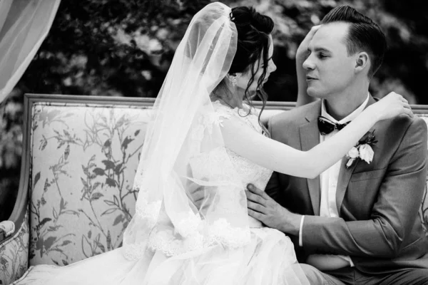 新娘和新郎坐在花园里的一张漂亮的沙发上 新娘穿着粉色蓬松的连衣裙新郎穿着灰色西服黑白照片 — 图库照片