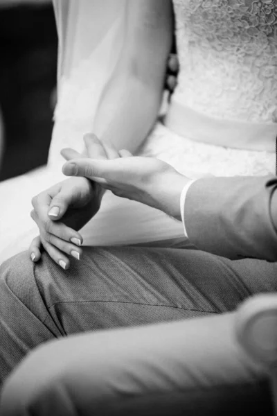 The bride and groom are sitting on a beautiful couch in a gazebo in the garden and holding hands. White tent. The bride in a pink fluffy dress, the groom in a gray suit. Black and white photo