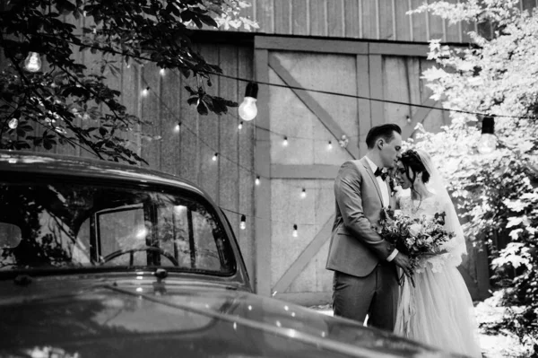 The bride and groom walk in the garden near the rarity car. Wedding in the forest. Black and white photo