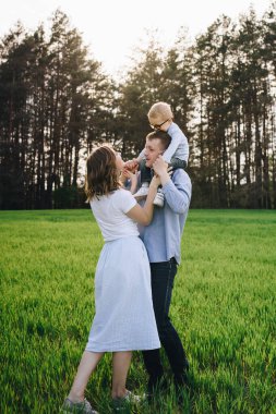 Ormanda piknikte bir aile. Açık bir alanda, yeşil çimlerde oturmak. Mavi kıyafetler. Anne ve baba oğullarıyla oynar, sarılır ve gülümserler. Gözlüklü bir çocuk..