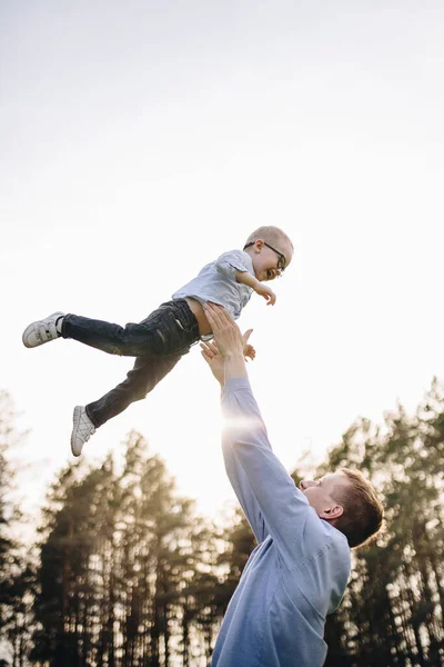 Family in nature. Picnic in the forest, in the meadow. Green grass. Blue clothes. Dad, son with glasses. A boy with blond hair. Joy. Dad throws his son in the air. Together.