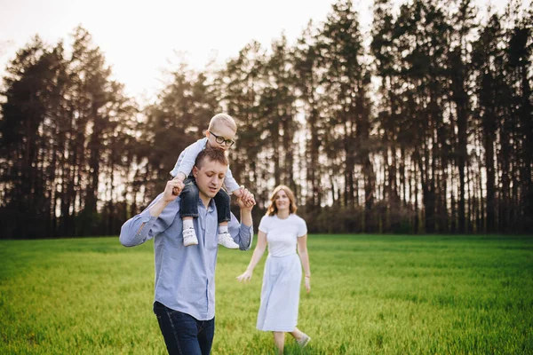 Family in nature. Picnic in the forest, in the meadow. Green grass. Blue clothes. Mom, dad, son with glasses. Boy with blond hair. Joy. Parents play with child. Together. Picnic basket. Food, blanket