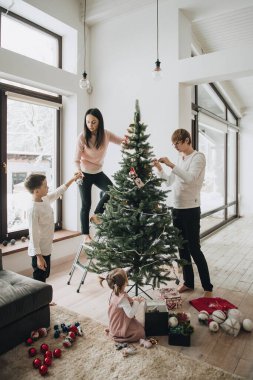 Yeni yıl. Noel ağacını süsleyin. Yapay ağaç. Pembe saçlı, at kuyruklu bir kız Noel ağacını süslüyor. Kutuda Noel oyuncakları. Tatil beklentisiyle. Aile bir arada. Işık odası.
