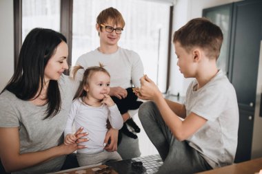 Aile mutfakta zencefilli kurabiye hazırlıyor. Baba, anne, oğul, kız, erkek ve kız kardeş. Diz hamuru, kurabiye kesiciler, yeni yıl, Noel, tatil yemeği. Gri ev kıyafeti.