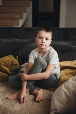 Büyük bir evde aile. Yaşam tarzı ev konforu. Evdeki çocuklar. Yerde oynayan çocuklar. Tekstil. Oğlan yerde oturuyordu. Kahverengi kanepe, sarı yastıklar. Bir çocuğun portresi.