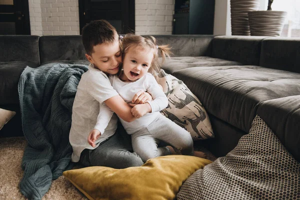 Family in a big house. Lifestyle Home comfort. Children at home. Children playing on the floor. Textile. Brother and sister hug. Brown sofa, yellow pillows.