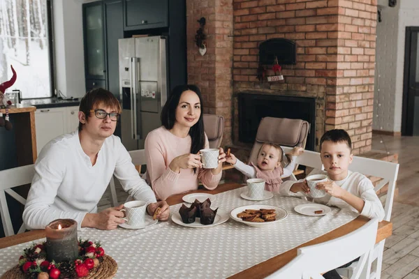 Family in a big house. Lifestyle Home comfort. Children at home. Beautiful kitchen. Children's diet. family has lunch together. Gingerbread cookie with tea. Red brick fireplace. Large dining table