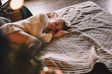 Yatak odasındaki yatakta yatan kız. İçi karanlık. Yeni yıl ve Noel. Beyaz kazak ve yüksek çoraplar. Romantik bir buluşma. Randevu aşıkları. Uzun saçlı güzel kız..