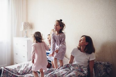 Çocuklar ve ebeveynler sabahları yatakta dinlenirler. Çocuklar şımarır, sarılırlar. İkizler. Üç kız..