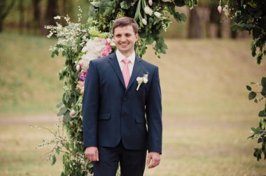 Klasik bir düğün. Gerçek çiçeklerden bir kemer. Gelin, damadı bekliyor..